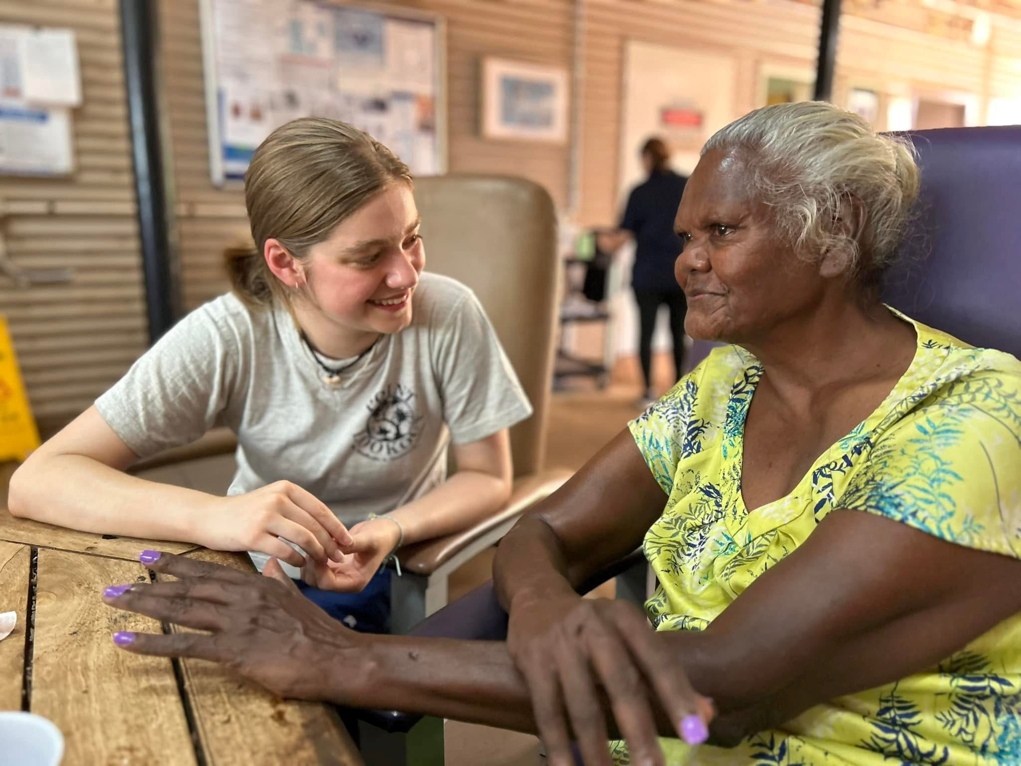 Student participating in a service learning initiative sits with a community member at a table, engaging in conversation and connection during an outreach activity.